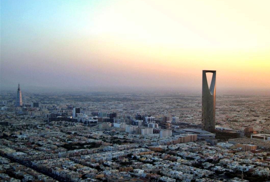 Aerial view of the Riyadh skyline at golden hour, with the Kingdom Tower and Al Faisaliah Tower rising above sprawling residential neighborhoods, illustrating Saudi Arabia's 2026 law allowing foreigners to buy freehold property.