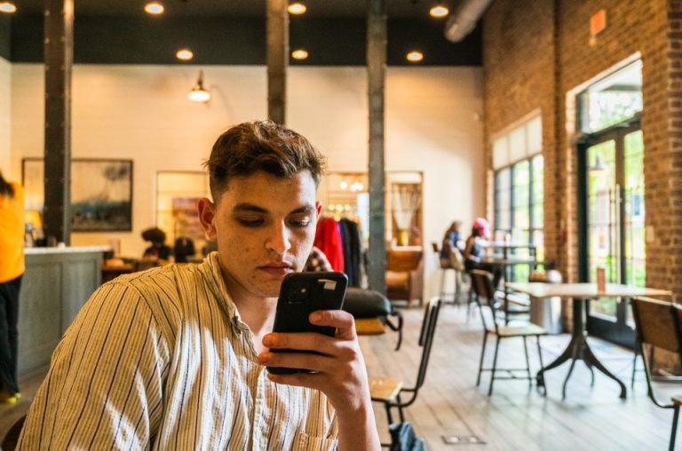 A man reading a message on his smartphone indoors, illustrating the risk of encountering the viral 'AED 100,000 lifetime Golden Visa' nomination scam and unauthorised paid-middleman fraud in the UAE.