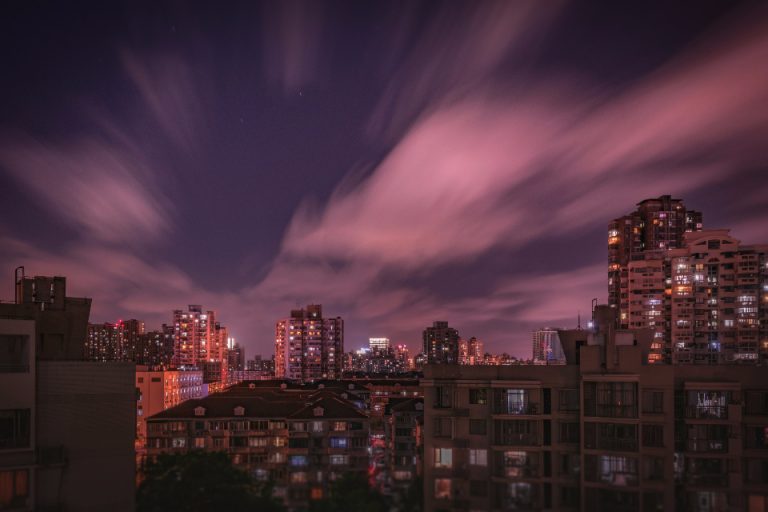 Dense high-rise residential towers forming a city skyline under a dramatic moody dusk sky, illustrating Kuwait's 2026 residency reforms including the KD 800 family-sponsorship salary rule and doubled iqama and insurance fees