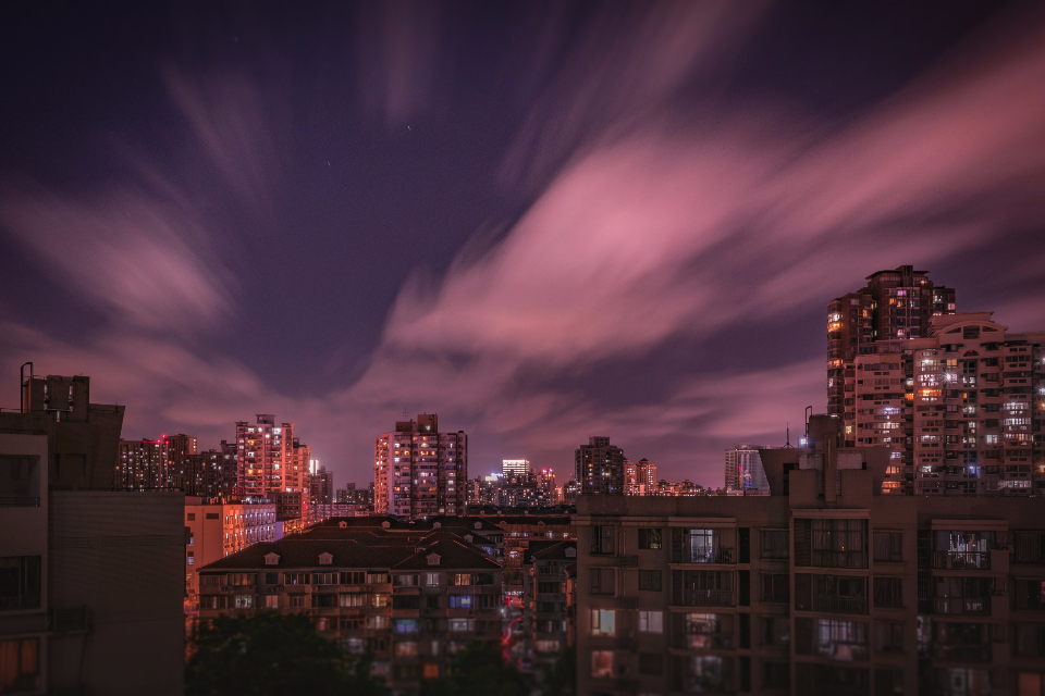 Dense high-rise residential towers forming a city skyline under a dramatic moody dusk sky, illustrating Kuwait's 2026 residency reforms including the KD 800 family-sponsorship salary rule and doubled iqama and insurance fees