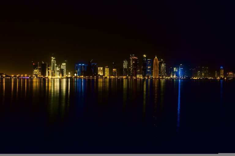 Night skyline of Doha's West Bay district with illuminated modern skyscrapers, used as a faded backdrop for a Qatar 2026 multi-sector jobs map