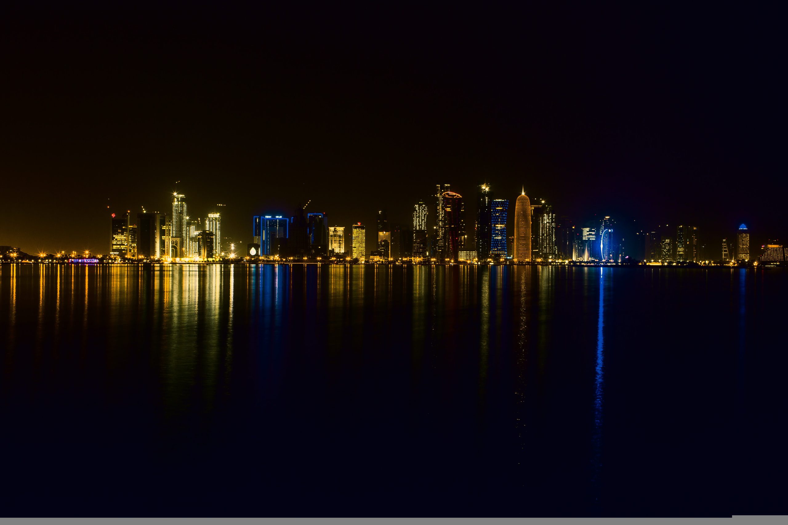 Night skyline of Doha's West Bay district with illuminated modern skyscrapers, used as a faded backdrop for a Qatar 2026 multi-sector jobs map