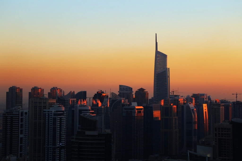 Dubai skyline silhouetted against a glowing orange sunset, representing the UAE's sponsor-free residency routes - the 5-year Green Visa, the 12-category Golden Visa, and the 10-year Blue Residency.