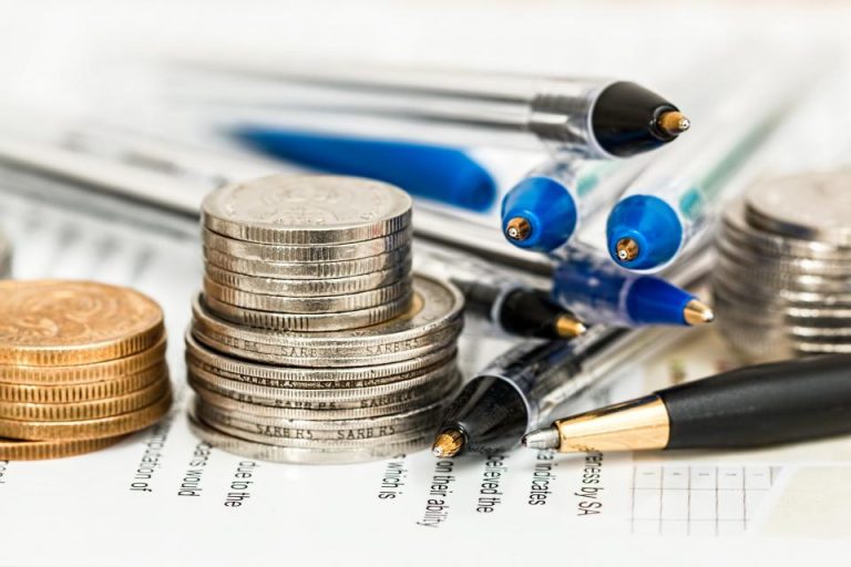 Stacks of coins of increasing height resting on a financial statement beside pens, illustrating an end-of-service gratuity lump sum being invested and growing under the UAE Voluntary Alternative End-of-Service Benefits savings scheme