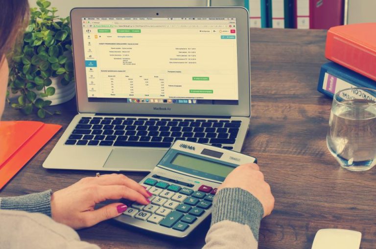 A person using a desk calculator while reviewing accounting and tax spreadsheets on a laptop, illustrating UAE corporate tax 2026 filing, the 9% rate calculation and the 30 September deadline